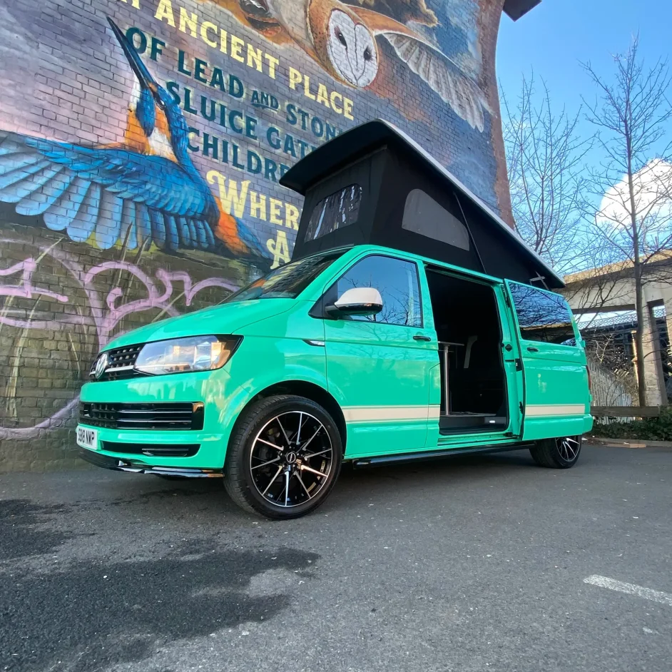 Green camper parked under a bridge with roof extended