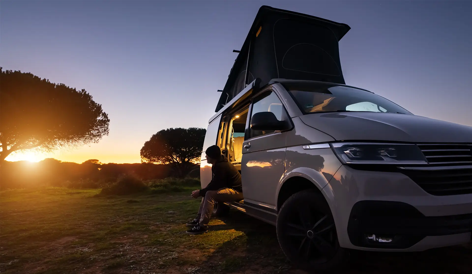 White camper at sunset in a field with rood extended