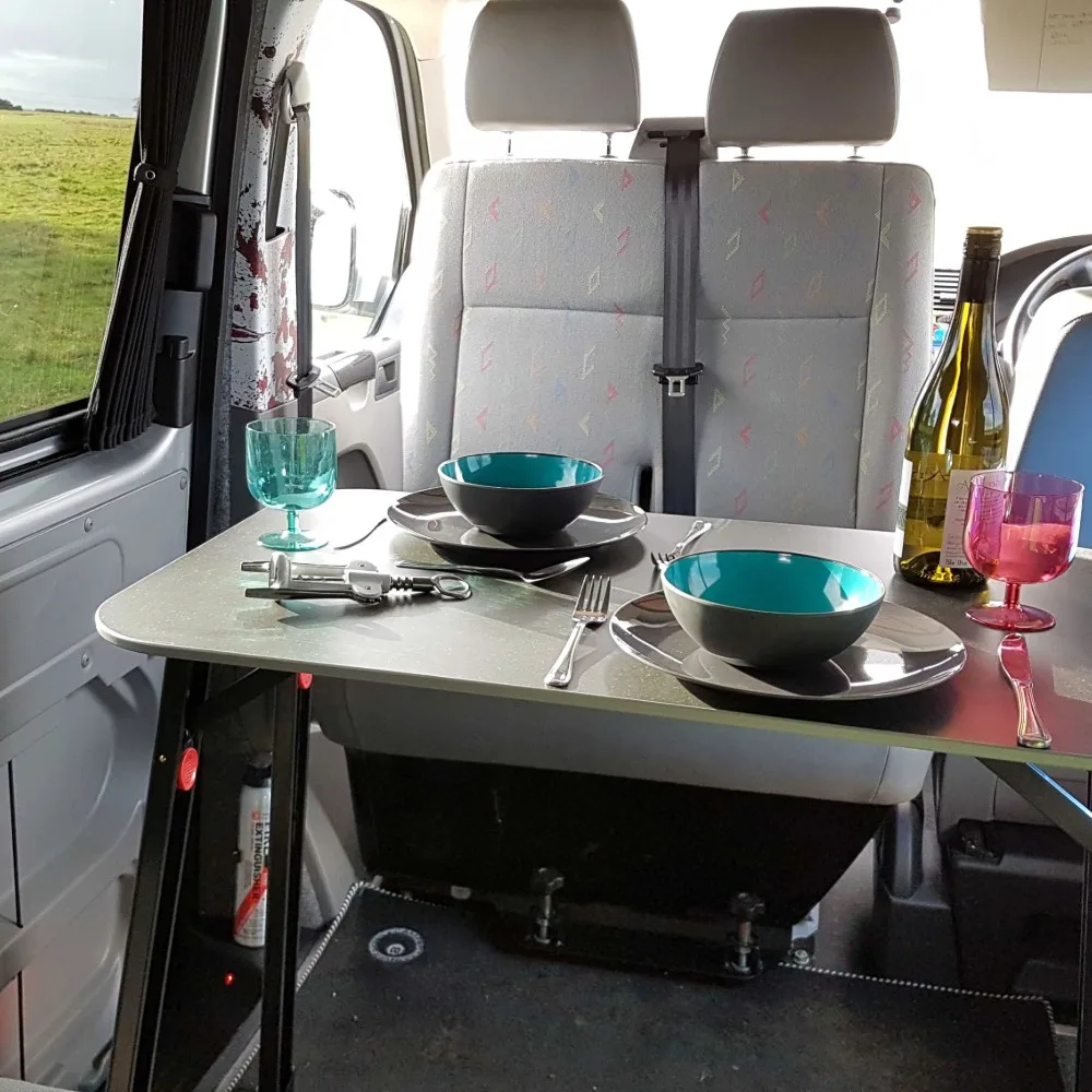 A small dining table in a camper van with a bottle of wine and colourful glasses.