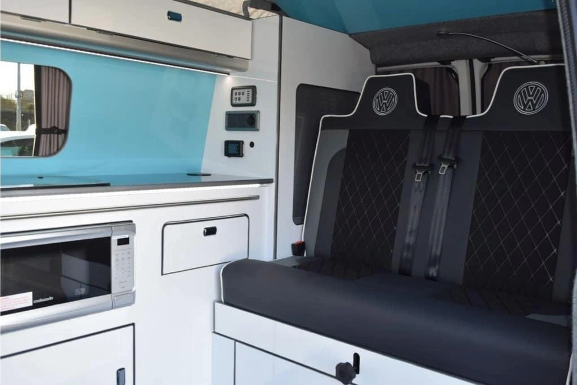 The interior of a modern VW camper van with a black, white, and light blue colour scheme.