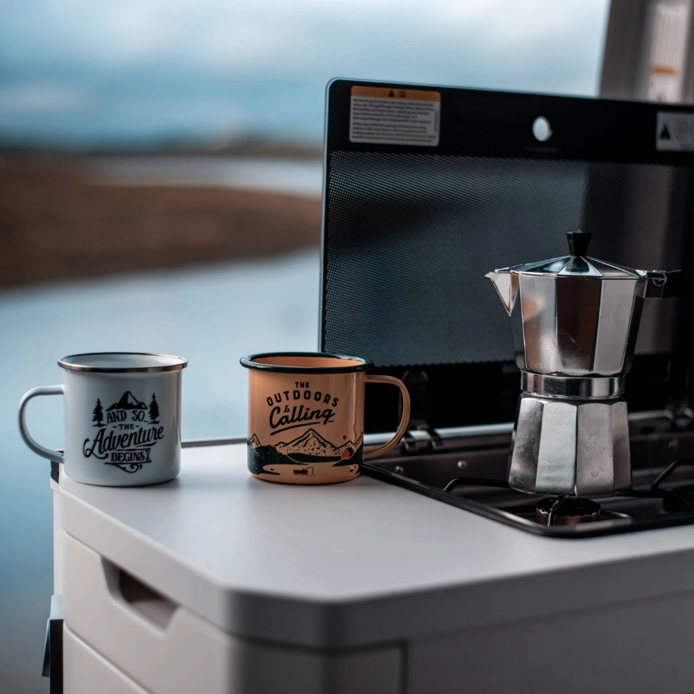 A kettle and mugs sat on a bench in front of a lake.