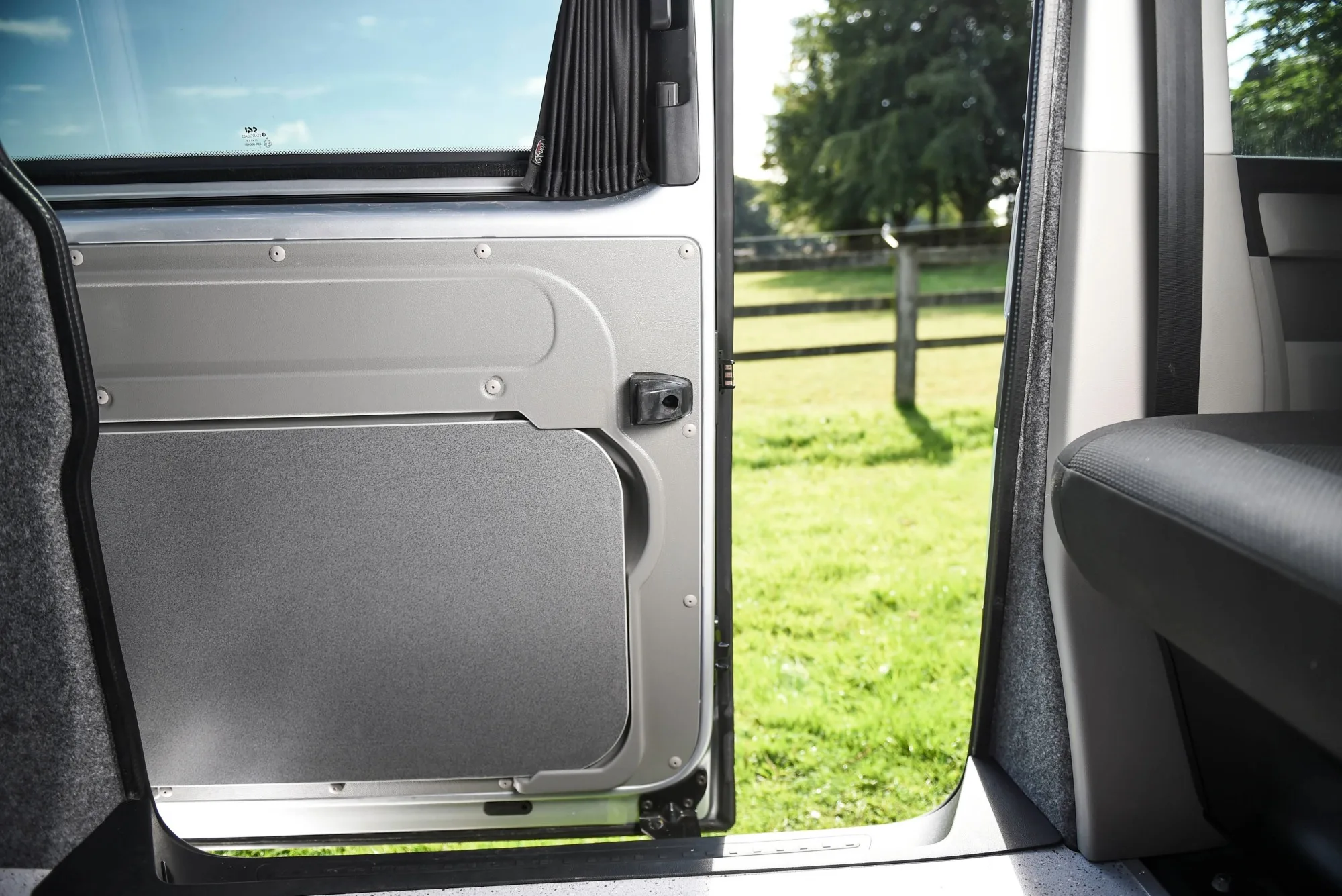 The sliding door of a small camper van reveals green fields.