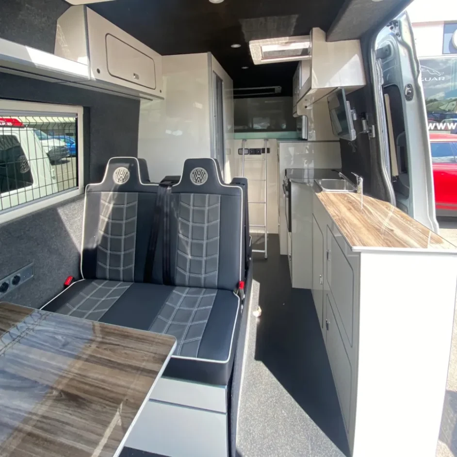 A spacious camper van interior with a wooden table and VW-branded chairs.