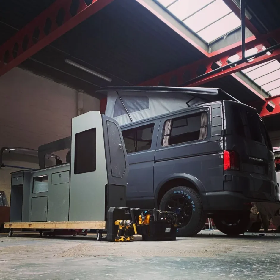 A camper van with a pop-top roof parked next to kitchen furniture.